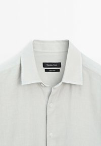 Light gray linen shirt with a crisp collar, front button closure, and a black label reading "Massimo Dutti." Soft texture and simple design.