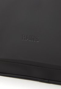 Schwarze wasserdichte Tasche mit subtiler Textur, featuring geprägtem "RAINS"-Logo. Glatte Oberfläche, minimalistisches Design, keine zusätzlichen Akzente oder Muster.