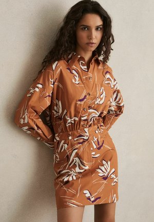 Bruine gebloemde jurk van katoen, met een kraag, lange mouwen, elastische taille en gedurfde witte en paarse bloemenprints.