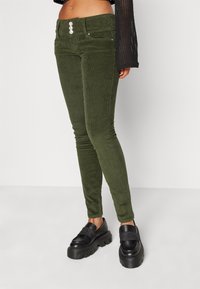 Olive green corduroy skinny pants with a high waist, three-button closure, front pockets, and a textured finish.