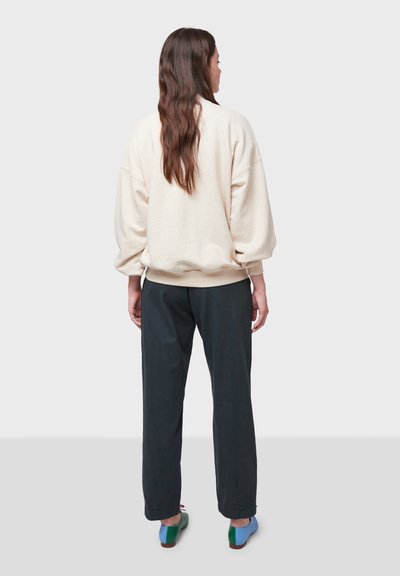 Felpa beige oversize con maniche ampie, abbinata a pantaloni scuri a gamba ristretta. Il modello indossa scarpe con tacco a blocco multicolore.