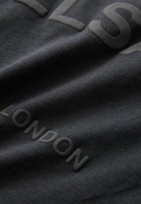 Must mustreid must must tekstiga "LONDON" ja osa teisest sõnast. Tekstuur on sile ja veidi elastne.