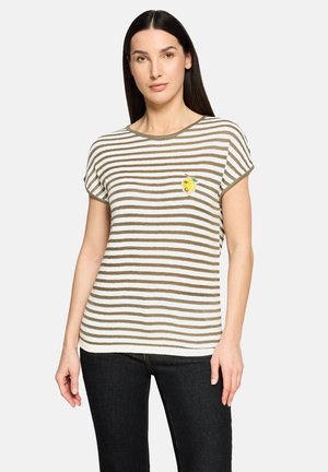 Woman with straight dark hair wearing a short-sleeve white and olive striped top with a small lemon patch on the chest and black pants.