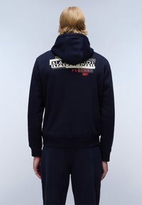 Navyblauwe hoodie met een zachte textuur, voorzien van een grafische print op de rug. Extra ontwerpelementen zijn een kangoeroezak en geribde manchetten.