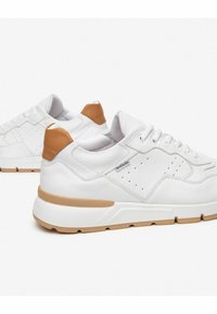 Hvide sneakers med brune accenter, der er lavet af glat lædermateriale, har perforeret design til ventilation og en struktureret gummisål.