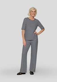 Gestreifter Jumpsuit aus marineblauem und weißem Stoff, mit kurzen Ärmeln und lockerer Passform. Auffälliges wellenförmiges Muster, kombiniert mit schwarzen Sandalen.
