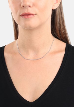 Collana in argento indossata su pelle nuda, caratterizzata da un design liscio e snodato; la persona che la indossa ha una maglietta nera a scollatura a V.