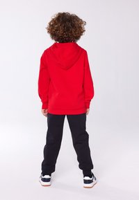 Sudadera roja con capucha, mangas largas y puños acanalados, combinada con pantalones de chándal negros y zapatillas blancas con detalles en azul marino.