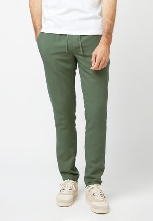 Grüne Baumwollhose mit schmalem Schnitt, ausgestattet mit elastischen Bündchen und einem Kordelzugbund, kombiniert mit beigen Sneakers.