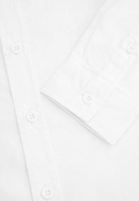 Biała koszula z wyrazistym kołnierzykiem, zapinana na guziki z przodu na cztery guziki oraz z guzikami przy mankietach, wykonana z teksturowanej bawełny.