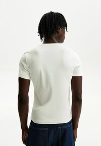 White fitted short-sleeve T-shirt with a ribbed texture, round neckline, and seamless design. Worn with dark denim jeans.