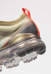 Air Nike Vapormax, tomaia in rete verde oliva, linguetta posteriore rossa, accenti neri, ammortizzazione traslucida, suola testurizzata con motivi di battistrada.