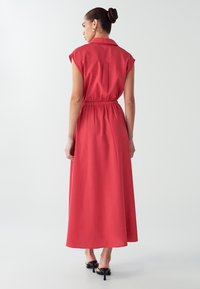 Rød, ærmeløs maxi-kjole med krave, indsnøret talje og flydende nederdel. Glat tekstur og minimalistisk design.
