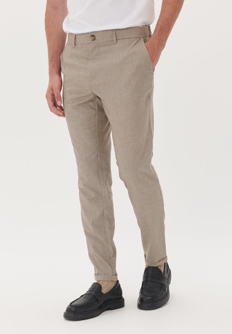 Beige op maat gemaakte broeken met een subtiele textuur, slim fit en een knoopsluiting bij de taille, gecombineerd met zwarte instappers.