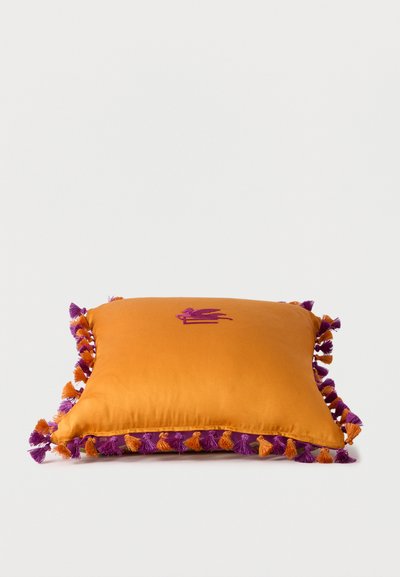 Coussin rectangulaire orange avec des pampilles violettes et orange le long des bords et un petit oiseau violet brodé au centre.