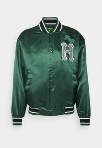 Grüne Satin-Bomberjacke mit einem schwarz-weißen gestreiften Rippsaum und Bündchen sowie einem auffälligen weißen "H"-Emblem auf der Brust.