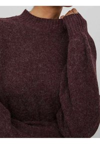 Hnědý pletený svetr s vysokým stojáčkem a žebrovanými manžetami. Tkanina působí měkce a chlupatě, s jemně strukturovaným povrchem.