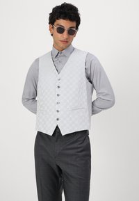 Hellgraue Weste mit strukturiertem Rautenmuster, sechs Knöpfen und zwei vorderen Taschen, kombiniert mit einem passenden Button-Up-Hemd und dunkelgrauen Hosen.