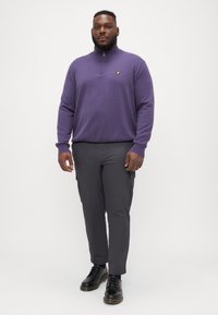 Purple zip-neck sweater with a small yellow logo, paired with gray cargo pants. Black lace-up shoes complete the outfit.