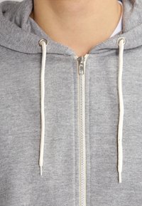 Grå zip-up hettegenser med myk tekstur, med hvite snorer, en metallglidelås og et enkelt design uten mønstre.