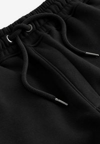 Black sweatpants made of soft fabric with a drawstring waist. Features metallic aglets and subtle textures on the surface.