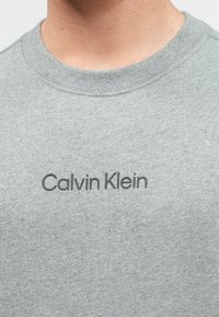 Γκρι βαμβακερό t-shirt με στρογγυλή λαιμόκοψη και κοντά μανίκια, με το λογότυπο "Calvin Klein" εκτυπωμένο σε σκούρο γκρι στο στήθος.