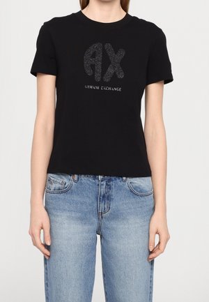 Kobieta ubrana w czarną koszulkę z krótkim rękawem z błyszczącym logo "AX Armani Exchange" oraz jasnoniebieskie, wysokie dżinsy.