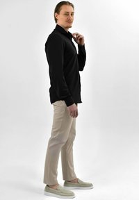 Zwarte lange mouwen shirt, beige slim-fit broek en lichtgroene suède instapschoenen. Glad materiaal en een getailleerde pasvorm met een subtiele kraag detail.