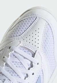 Zapatilla deportiva blanca con upper de malla texturizada, acentos de cuero suave, detalles perforados y logotipo gris contrastante.