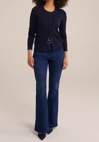 Marinblå stickad cardigan med rund halsringning, framknäppning och strukturerat mönster, parat med högmidjade utsvängda jeans och mörka klackar.