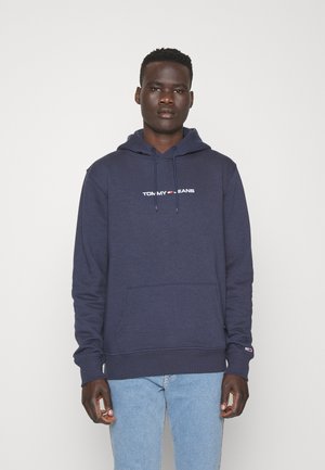 Sudadera color azul marino hecha de una tela suave, con un bolsillo frontal, capucha con cordón ajustable y texto de logo en blanco en el pecho.