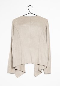 Beige mocka jacka med långa ärmar, ryggslits och asymmetrisk fåll. Slät yta och rena linjer, hängande på en svart krok.