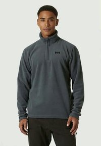 Pulôver de fleece cinza, com fecho zip e mangas longas, e um colarinho alto. Apresenta um pequeno logótipo preto no peito. Tecido texturizado.