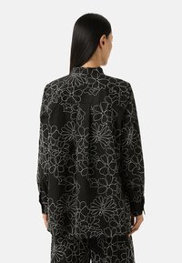 Black button-up shirt displaying white floral outlines. Features a back yoke and long sleeves with cuffs. Lightweight fabric with a relaxed fit.