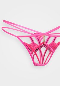Roze kanten string met ingewikkeld geometrisch ontwerp, doorzichtige gaaspanelen, verstelbare banden en gouden accentdetails aan de achterkant.