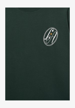 Tissu vert foncé avec un logo ovale brodé blanc contenant les lettres stylisées "L" et "A" et une petite étoile orange au centre.