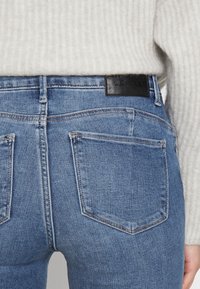 Jeans de denim azul de cintura alta con una textura suave, que presentan un parche de logo de cuero negro en la parte posterior y dos bolsillos traseros.