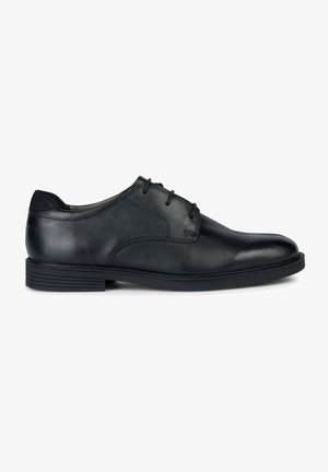 Zapato de vestir de cuero negro con punta redondeada, diseño con cordones, textura suave y un tacón de goma bajo. Presenta detalles de costura sutiles.