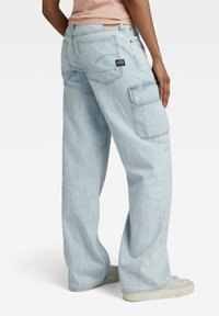 Lichtblauwe cargo jeans met een losse pasvorm, voorzien van grote zijzakken, een merklabel op de achterkant en subtiele stikdetails.