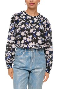 Bloemige blouse in zwart, blauw en wit met een gerimpelde halslijn en lange mouwen. Gecombineerd met lichtblauwe, glanzende denim jeans.