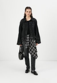 Giacca in denim nera con maniche lunghe, top nero, camicia a quadri legata in vita, jeans scuri e una borsa nera con borchie. Scarpe nere completano il look.