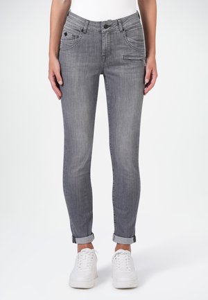 Slim-fit grijze jeans met opgerolde pijpen en ritszakdetail, gedragen met witte sneakers en een wit topje.