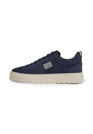 Navy blue suede sneaker with beige thick rubber sole, lace-up front, and rectangular branded patch on side, shown in side profile.