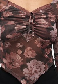 Αέρινο διαφανές τοπ με λουλουδάτο δίχτυ, ζωνάκι με ραβδώσεις στη μέση και δαντέλα περιμετρικά, με μεγάλα ροζ και μωβ λουλούδια σε σκούρο ύφασμα.