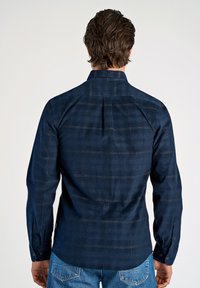 Marineblauwe button-upshirt met een textuurstof, subtiel ruitpatroon, schouderpas en ronde manchetten, gecombineerd met denimjeans.