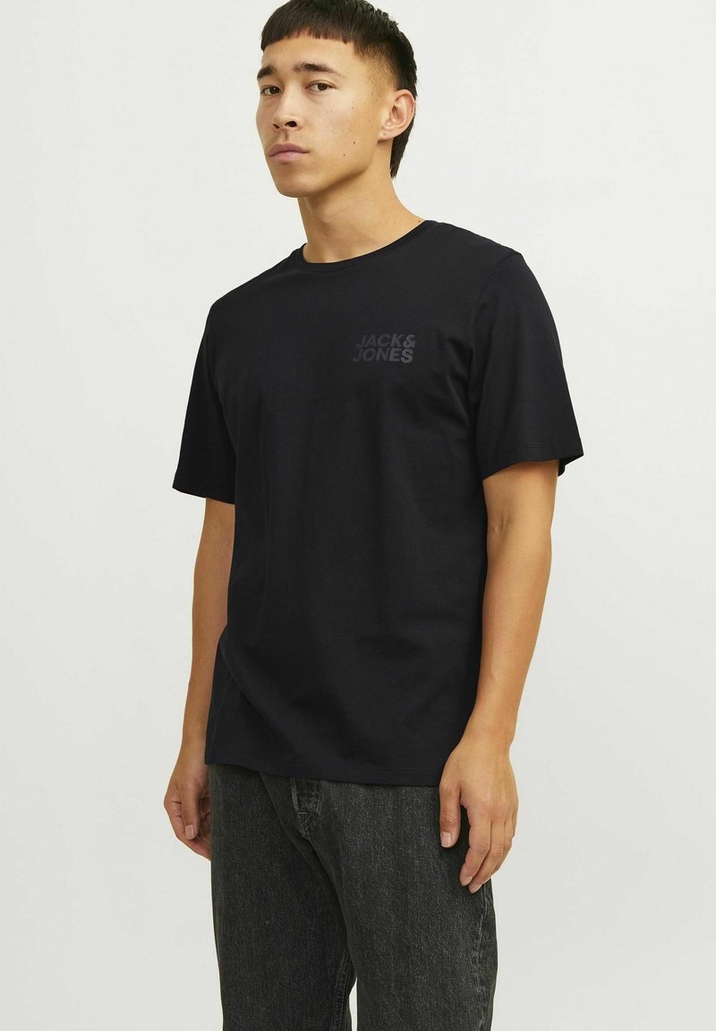 Schwarzes Baumwoll-T-Shirt mit kurzen Ärmeln und Rundhalsausschnitt. Verfügt über das dezente "JACK & JONES"-Logo im Brustbereich. Getragen mit dunkelgrauer Jeans.