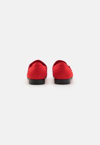 Rote Wildlederschuhe mit runder Zehenpartie, niedrigem schwarzen Absatz und einer glatten Oberfläche. Die Rückansicht betont das minimalistische Design und die klaren Linien.