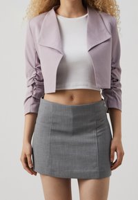 Chaqueta corta de color lila con mangas fruncidas, combinada con un top corto de canalé blanco y una falda mini gris ajustada. Tejido suave, diseño simple.