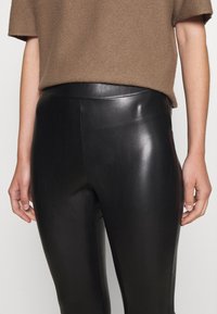 Svarta skinnleggings med en slät, blank yta, hög midja och en figurnära silhuett som formar benen.