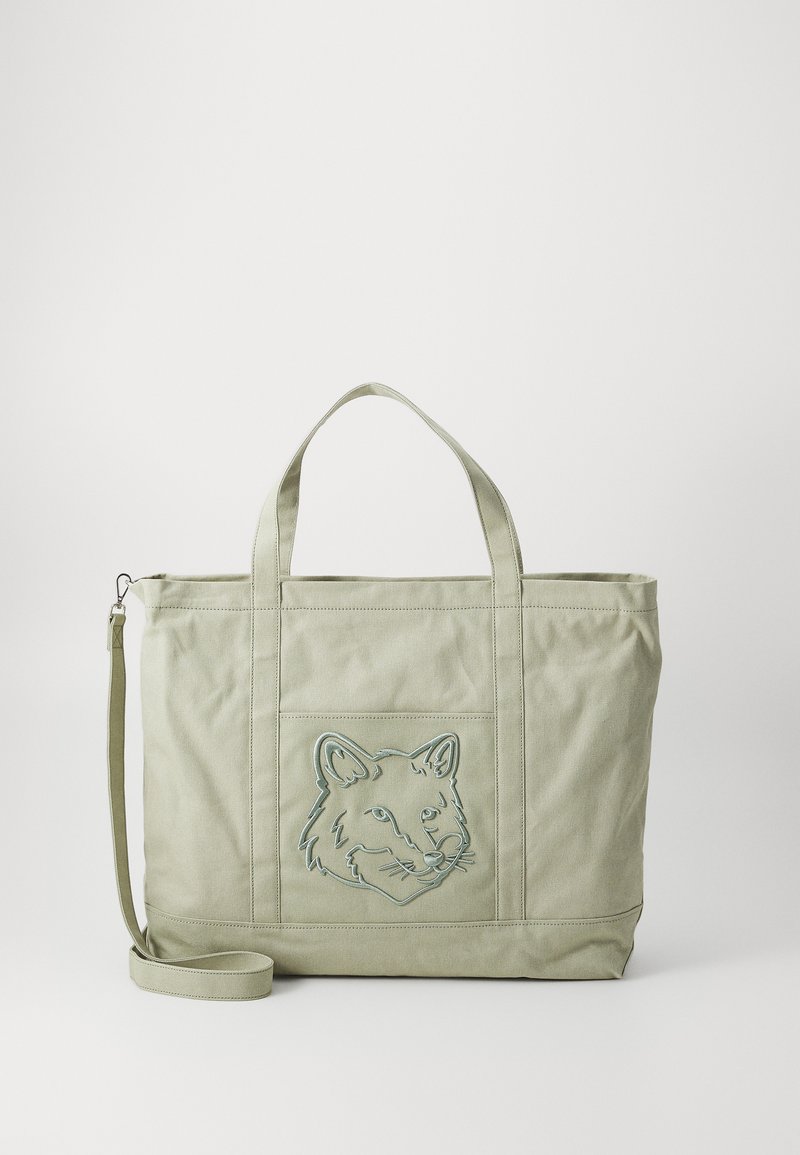 Bolsa de lona verde con un diseño bordado de la cara de un zorro. Cuenta con dos asas resistentes y una correa de hombro ajustable. Textura suave.